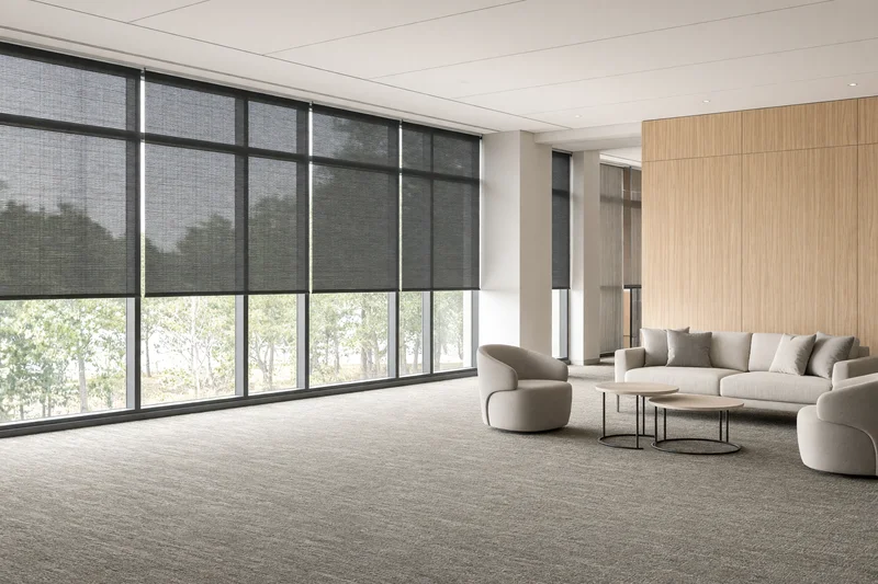 Illustration: a bright office common area with solar-screen roller shades across a glazed wall.